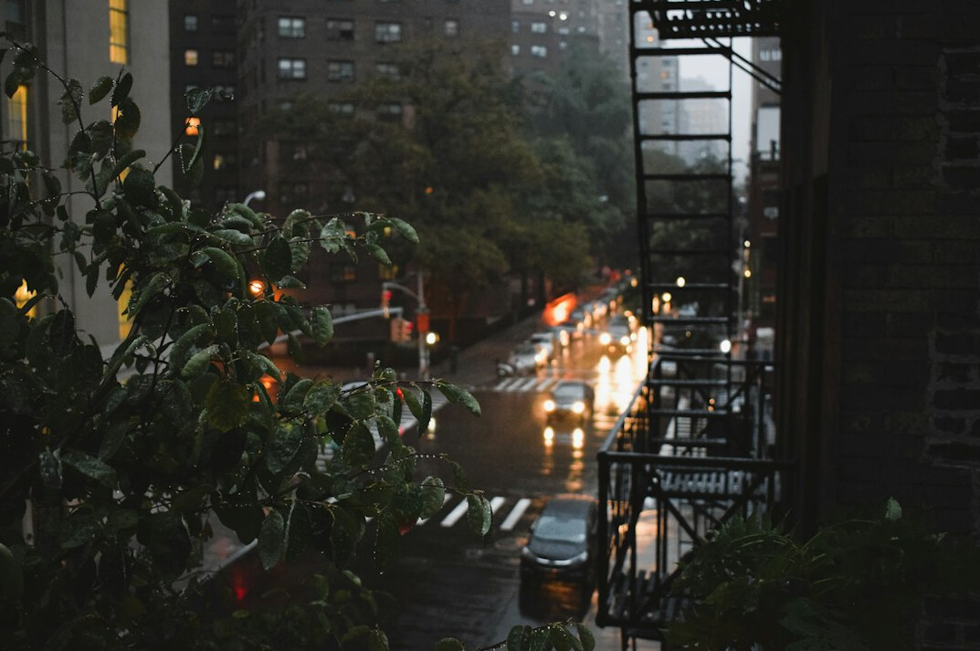 Rain-streaked window overlooking a city street with warm lit windows at night