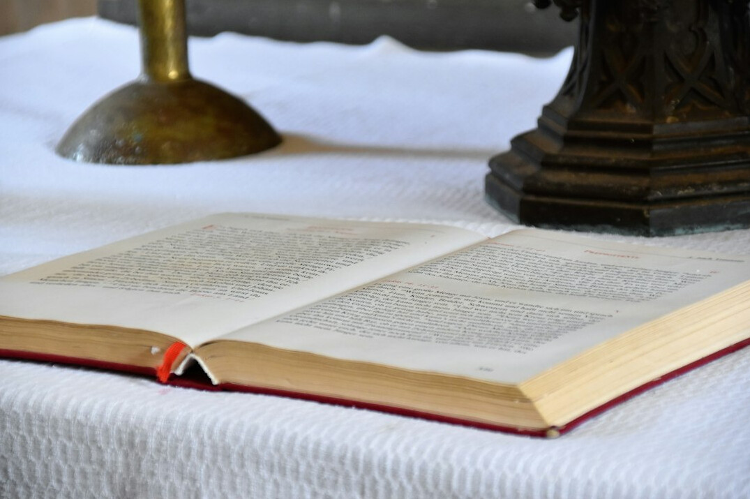 Open hardcover book beside a lit candle and antique pocket watch on a wooden table